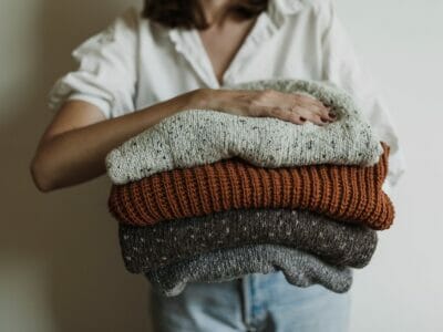 woman holding pile of knitted sweaters